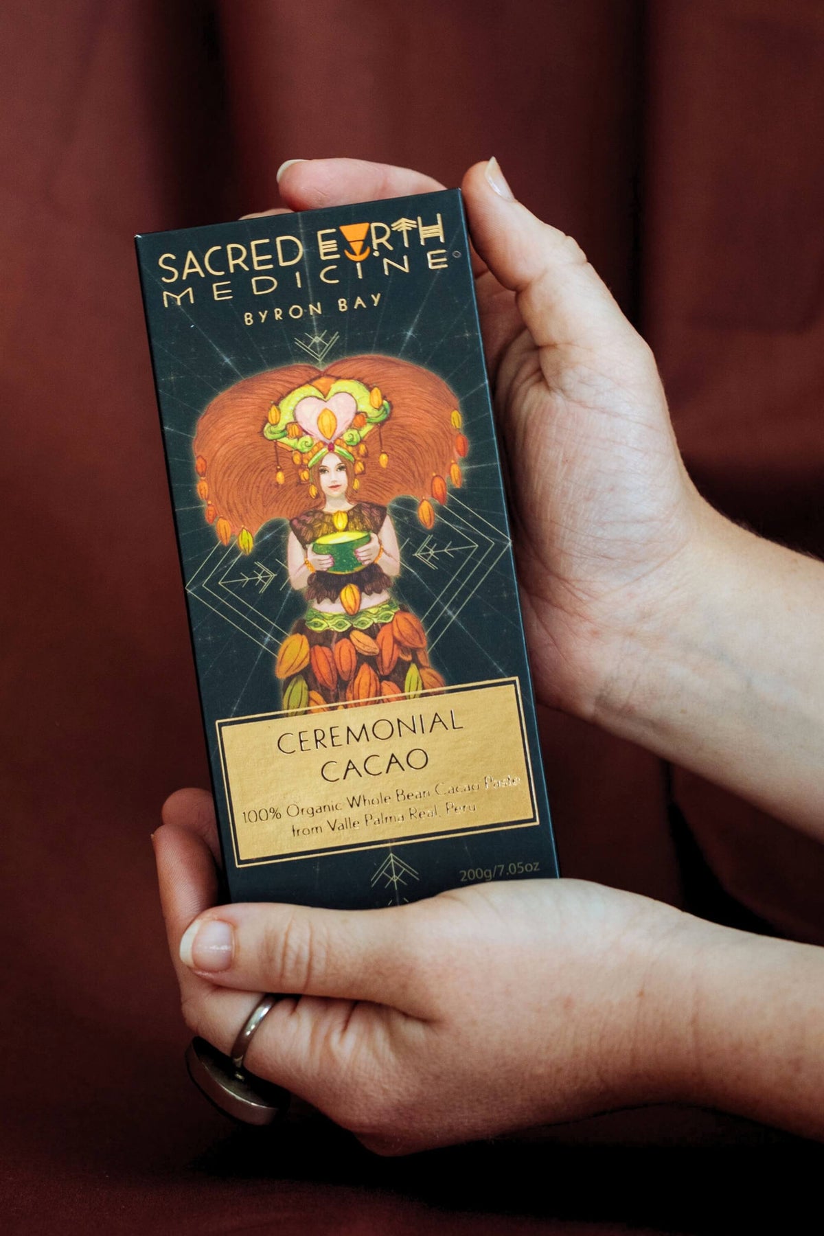 Hands holding a 200g block of Sacred Earth Medicine Ceremonial Cacao showing the front of the pack with the Cacao Goddess steeped in sacred geometry