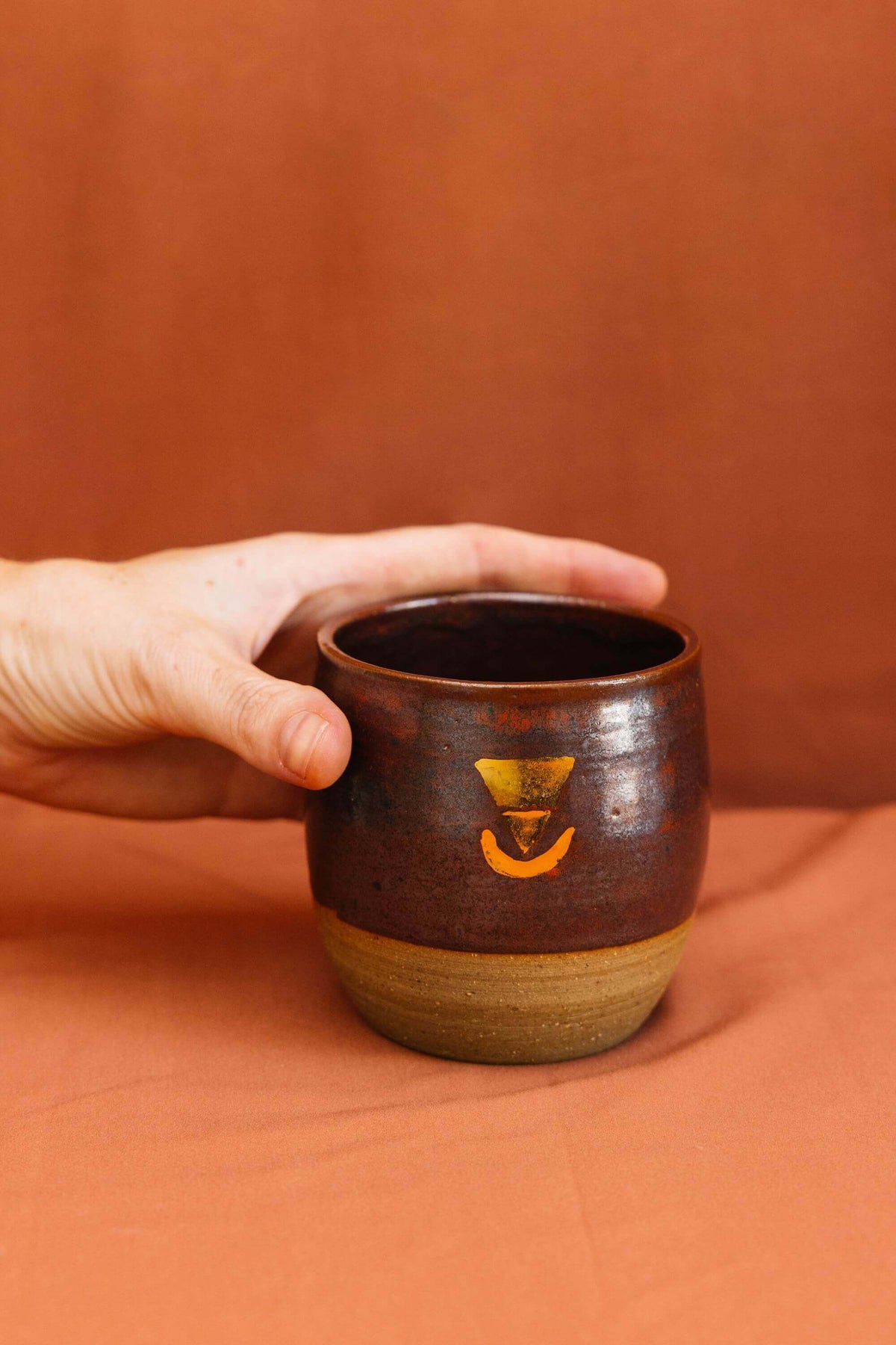 Hand holding a large ceremonial cup, embossed with a real gold lustre Sacred Earth Medicine symbol. The cup is made from wild harvested clay sourced using methods taught by the indigenous people from the Northern Rivers of NSW.