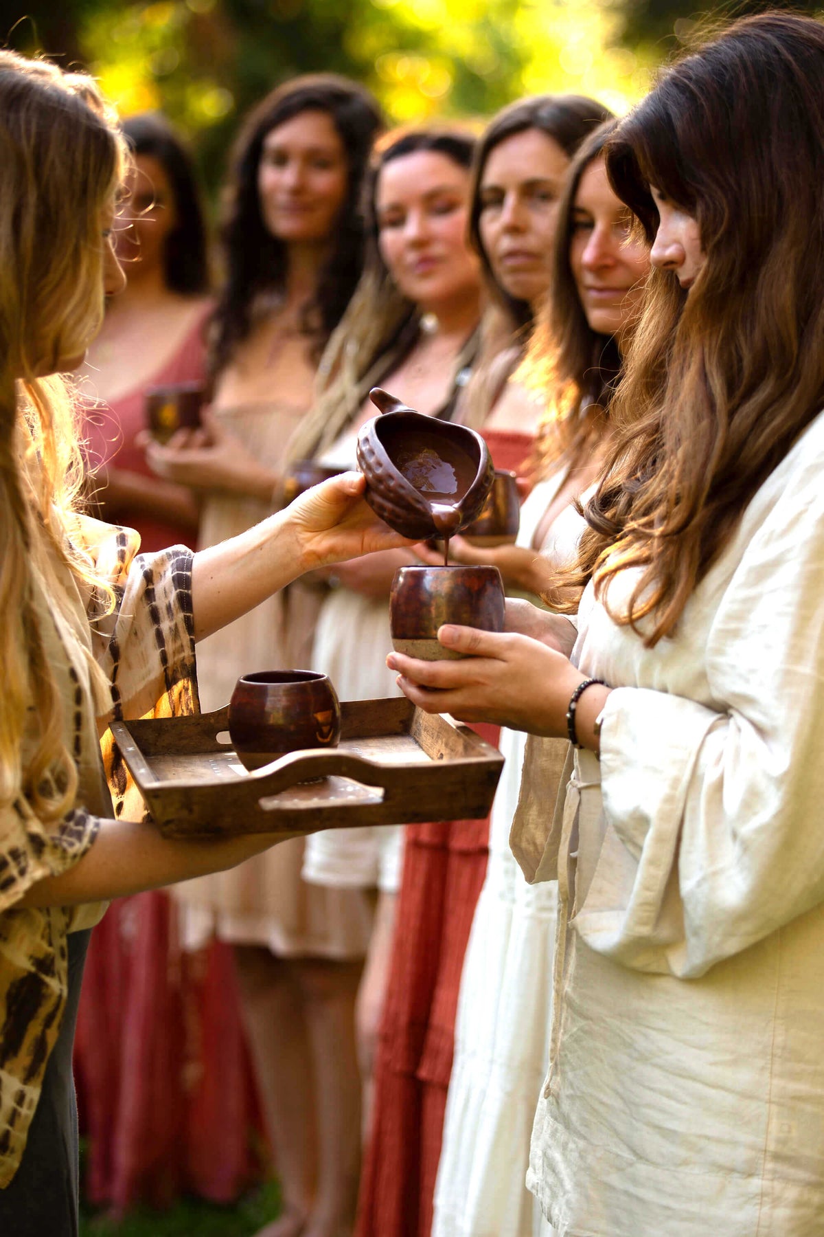 Serving Sacred Earth Medicine Ceremonial Cacao to a group of women as part of a sacred cacao ceremony. Each cacao cup is being poured from a clay cacao pod vessel.