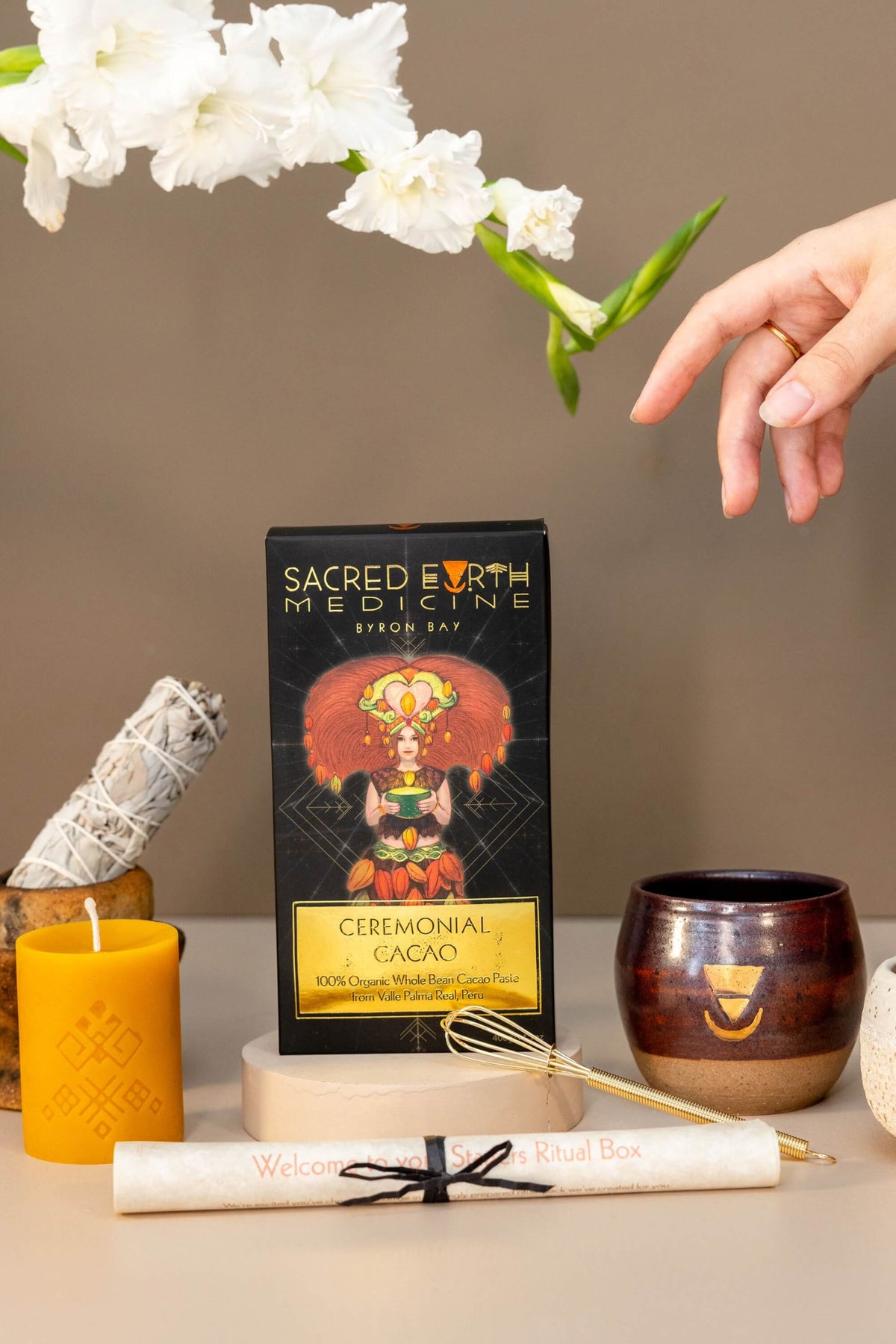 The complete contents of the Sacred Earth Medicine Starters Pack Ritual Box. A 400g block of SEM Ceremonial Cacao, 1 small ceremonial cup, a beeswax candle by Ahana, a sage stick, a whisk and a scroll to guide your through your very first Ceremonial Cacao experience. This makes a great gift! 